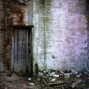 Old wooden doorway beside a whitewashed brick wall and scattered rubble