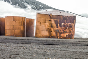 Large orange oil tanks with faded graffiti beneath an Antarctic hillside
