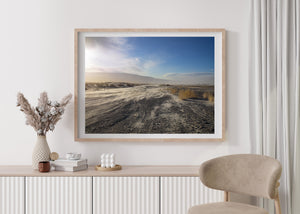 Wind lifted sand beside dry grasses and distant desert mountains