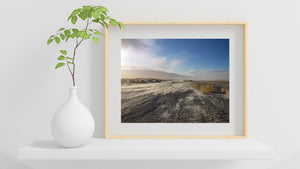 Sunlit sandstorm drifting across a road in an open desert landscape