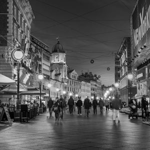Monochrome Zagreb street scene with pedestrians and rows of glowing lamps
