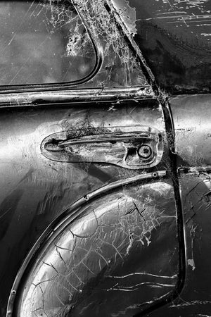 Black and white close-up of a vintage car door handle, worn chrome and curved trim.