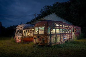 Colour photograph of weathered trolley cars standing in grass under a dark blue sky.
