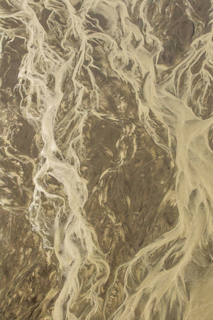 Vertical aerial landscape of Alaska’s exposed coast with pale waterways and soft earth tones.