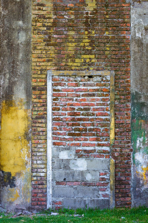Red bricks and grey blocks fill an old doorway surrounded by peeling coloured paint.