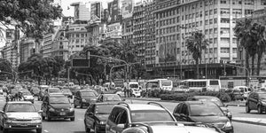 Autos und Busse füllen eine breite Allee in Buenos Aires unter Reihen von Stadtgebäuden.