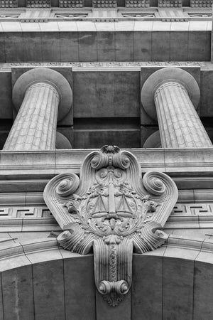 Columnas clásicas y balanzas de piedra talladas en una fachada de Buenos Aires, en blanco y negro.