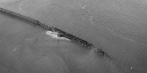 Un largo caballete industrial corta en diagonal el agua suavemente ondulada en monocromo.