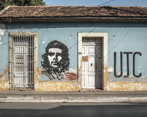 Un visage peint de Che Guevara se trouve entre une fenêtre à barreaux et une porte pâle dans une rue cubaine.