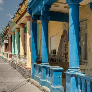A row of colourful Cuban house porches recedes along a bright pavement.