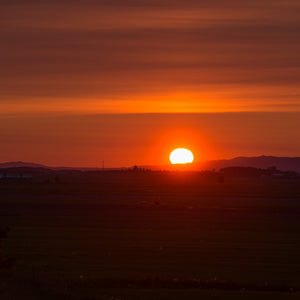 Thin horizontal clouds cross an orange sunrise over distant hills in rural Quebec.
