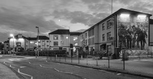 Illuminated murals beside an empty Bogside road beneath an evening sky in Derry.