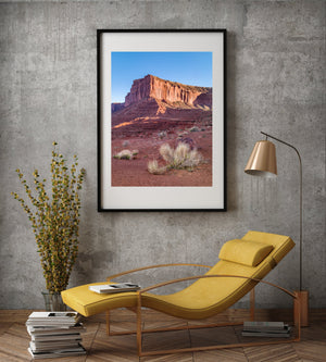 Scogliera di arenaria illuminata dal sole sopra radi arbusti chiari in una fotografia a colori del deserto.