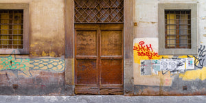 Panorama-Straßenszene in Florenz mit einer verwitterten Holztür, bunten Graffiti und Papierschildern.