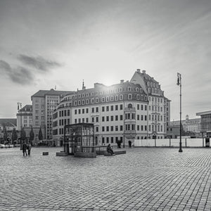 Sunlight breaks over ornate German rooftops above a broad stone-paved square