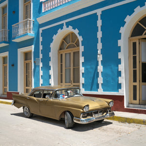 A vintage gold car stands beneath white-trimmed arches on a Cuban street