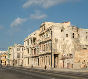 Fachadas frente al mar de La Habana con yeso descascarado, balcones y farolas ornamentadas en una luz dorada.