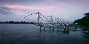 Row of traditional fishing nets above blue coastal water in Kochi