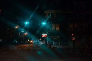 Green traffic signals cast turquoise light over a dark Medfield intersection