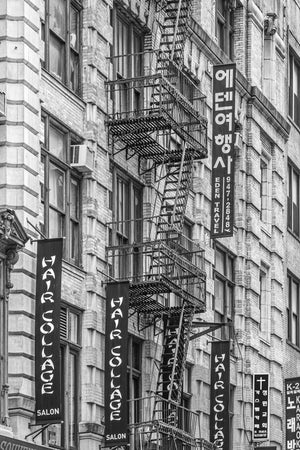 Metal fire escapes cross a brick facade beside Korean and English shop signs
