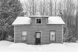 Fotografía invernal en blanco y negro de una antigua casa rural debajo de árboles nevados