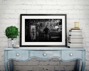 Black and white Cuban bar photograph with bottles, an old cash register and hanging currency.