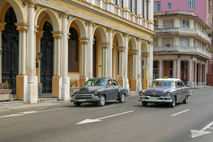 Colour Havana street photograph with vintage cars beside repeated cream arches.